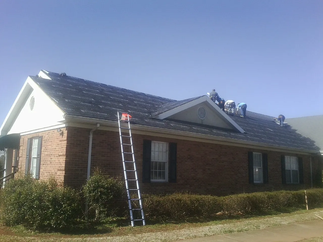 Crew tearing shingles off a brick ranch roof with a ladder set — Metal Roof Repair work by our crew in Cub Run