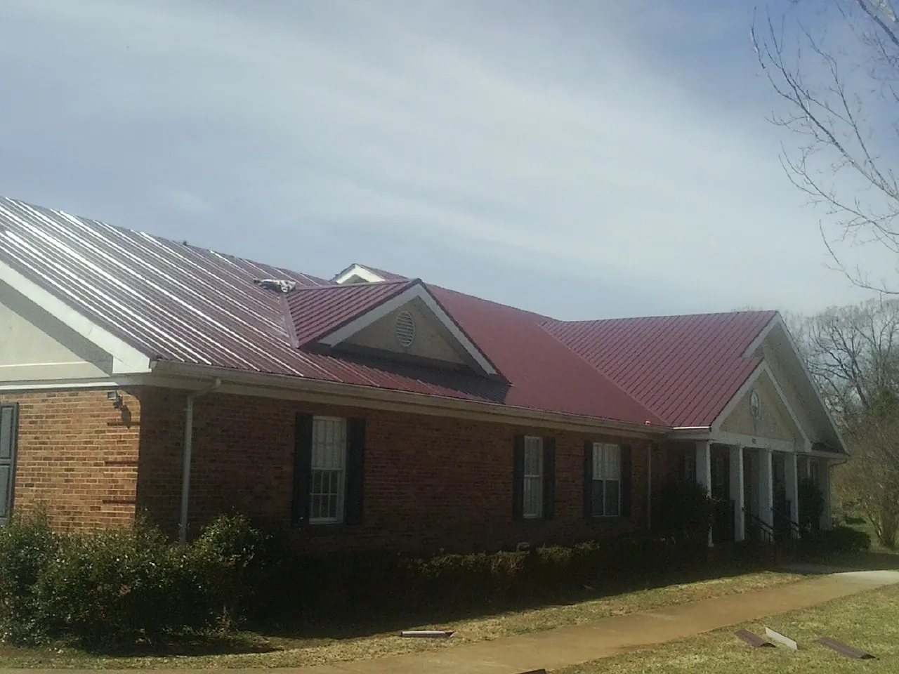 Red metal roof with gabled entries on a long brick building, from a Hail Damage Roof Repair job in Cub Run