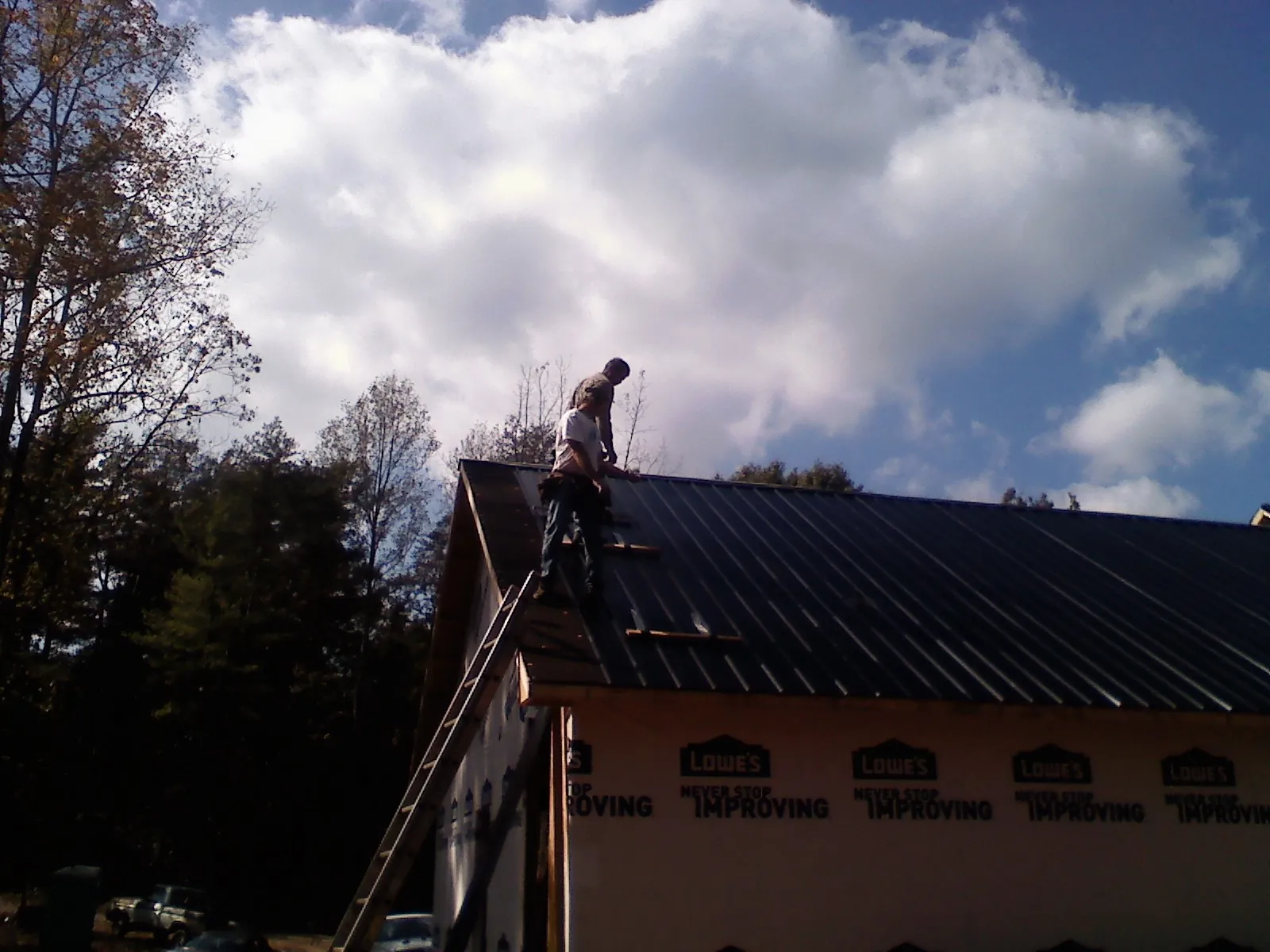 Roofer fastening dark metal panels high against a cloudy sky, from a Roof Inspection job in Cub Run