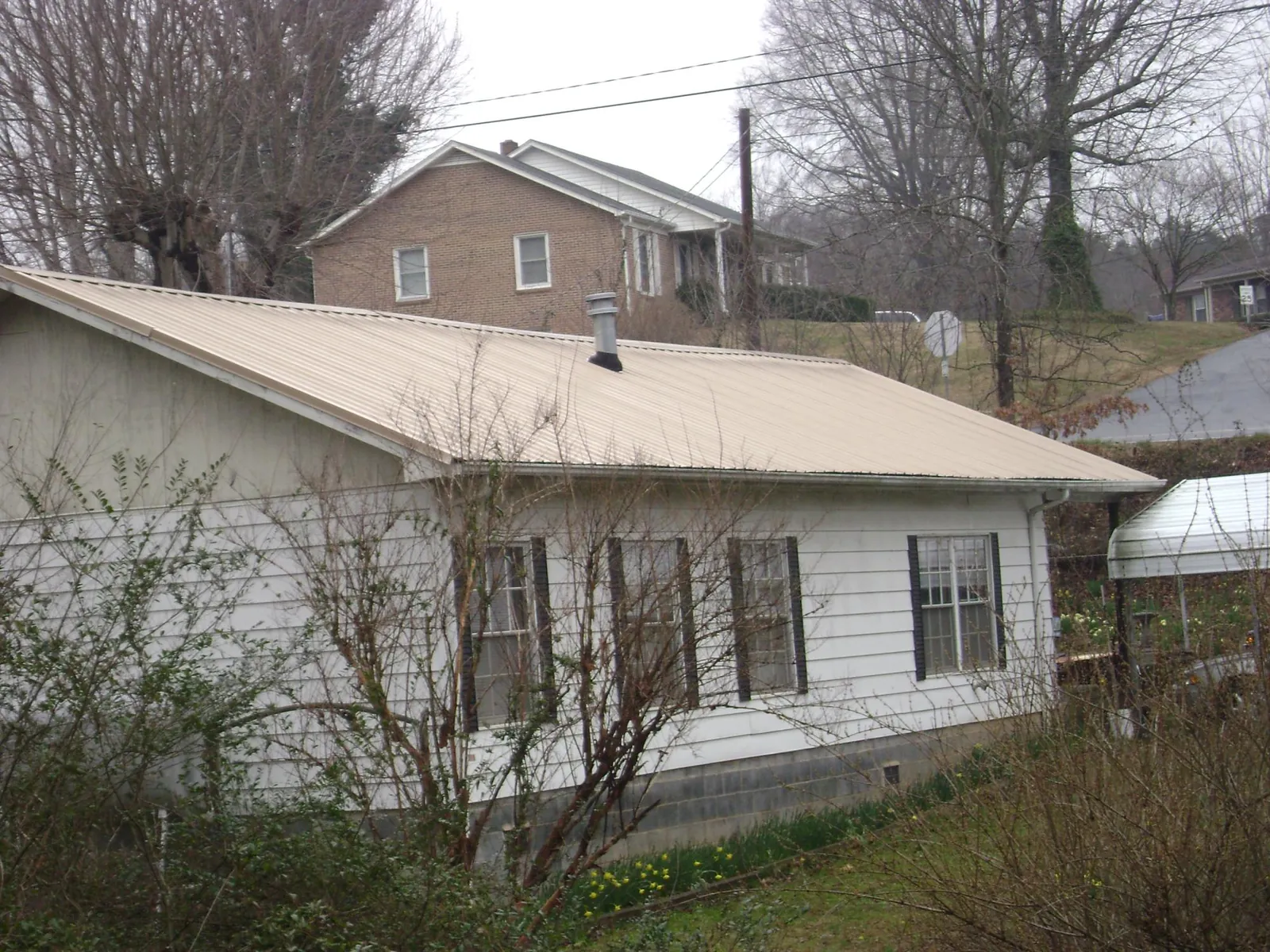 Tan metal roof on a white sided house set into a hillside — Commercial Roofing by Roofing Brothers in Cub Run